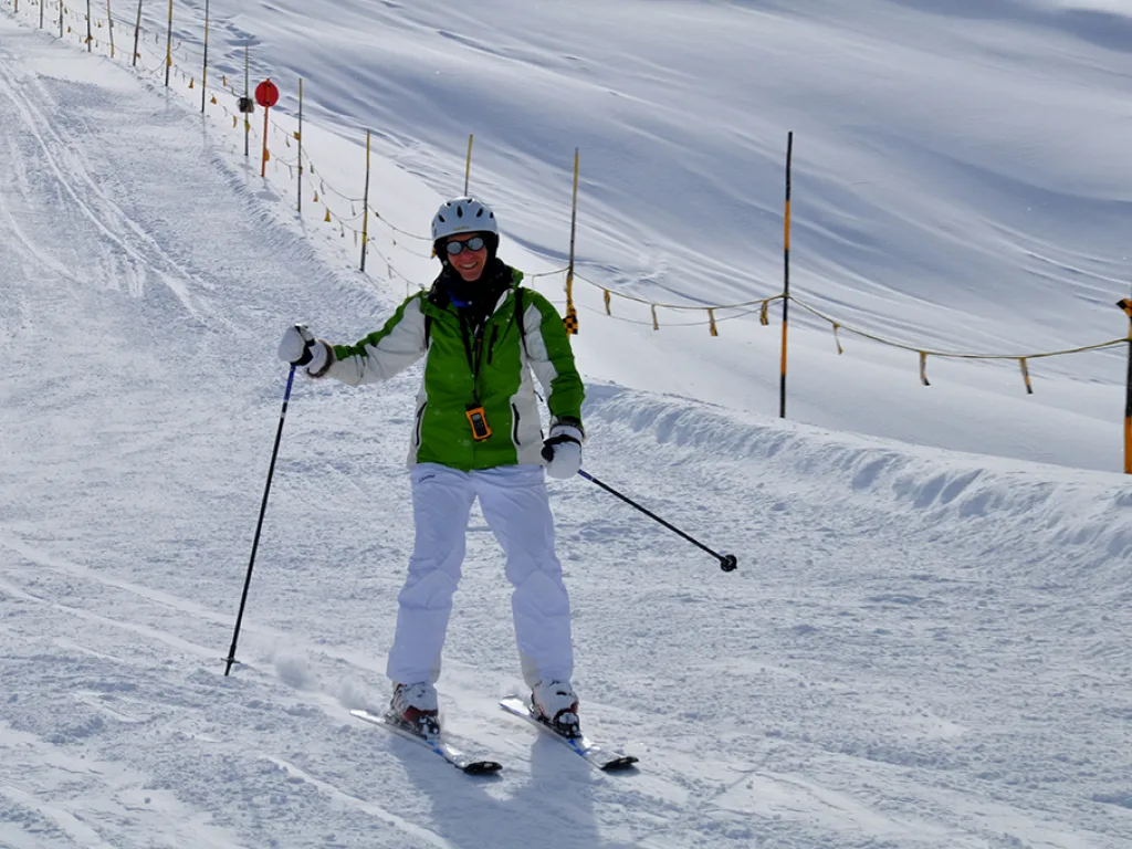 Skifahrerin in grüner Jacke steht am Pistenrand.